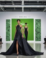 A fashion model walks down a runway in a high-fashion ensemble featuring a white dress with bold bla
