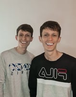 two men standing next to each other in front of a white wall