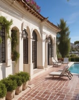 A luxury white villa with large windows and a green roof is situated on a scenic hillside. A man in sunglasses and swimwear is casually seated on a wooden railing, enjoying the warm sun.