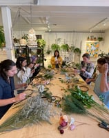 a group of people are gathered around a table during a wreath workshop