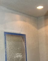Wall surface with fresh texture spray during interior paint prep, blue painter’s tape and plastic 