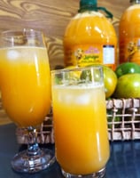 Taças de suco de laranja sobrepostas em uma mesa. Ao fundo, garrafas de suco de laranja.