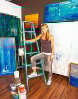 a portrait of a woman in a brown tank top and jeans standing on a ladder