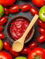 a bowl of tomato sauce with tomatoes and a wooden spoon