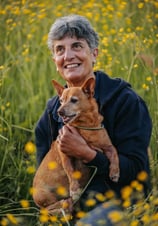 signora-anziana-che-abbraccia-un-cane-in-un-campo-di-fiori-gialli