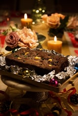 A chocolate cake with cashews on a candle-lit table decorated for Christmas with flowers and ribbons