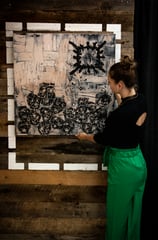 A female curator hangs a black-and-white painting to a wooden exhibit wall to cast proper lighting