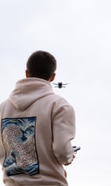 a man in a hoodie controlling a drone flying in front of him