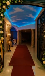 Pasillo elegante de Magic Party con techo iluminado tipo cielo, alfombra roja y decoración floral.