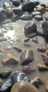 water glistens in the sun with colorful rocks in a pool 