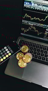 Cryptocurrency coins and smartphone calculator on a laptop showing Bitcoin trading charts.