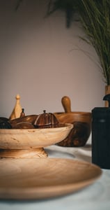 Objets artisanaux en bois posés sur une table : plat en bois clair sur pied rempli de fruits décorat