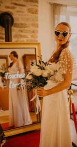 Une femme en robe de mariée qui pose devant le photobooth de pixtoevent avec des fleurs dans la main