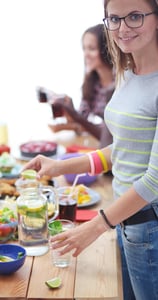 Vrouw die voor een tafel staat met een gezonde salade, symbool voor gezonde voeding of lifestyle.