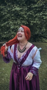 Femme rousse riante et joyeuse dans une robe violette et blanche dans un fond verdoyant
