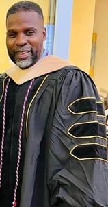 Dr. Marlon Ware standing and smiling in his graduation gown