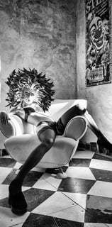 Belle jeune femme en sous vetements et bas noirs portant un masque vénitien dans un fauteuil 