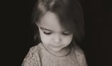 Two-year-old girl looking down thoughtfully against a black backdrop during a personality portrait s