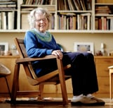 Naoma Powell, one of our founders, sitting in a chair she made, smiling at the camera.