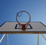 Low‑angle view of a weathered basketball hoop mounted on a white backboard against a clear blue sky