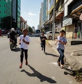 Childrens running down a street during a sunny day in Phnom Penh, Cambodia - by ACAT PHOTOS