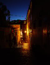 Night cobblestone alley lit of Lisbon by warm streetlights with walking silhouettes, By ACAT Photos