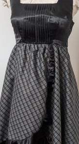 The front of a black/gold plaid and black satin flowy cocktail dress