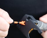 A close-up of a golfer's hand placing an orange golf tee into a 'TeeZup' tool attached to a club grip.