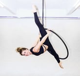 Vrouw in zwarte outfit voert een aerial hoop oefening uit bij De Polecats Fabriek in Gent