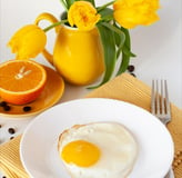 Fried egg, juicy orange, bouquet of yellow tulips, yellow napkin and fork