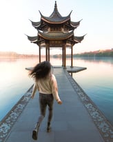Woman running down the path at the leifeng pagoda viewing point. There is a beautiful lake landscape with autumn colours.