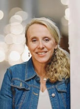 Owner Chris Bisner smiles while leaning against a wall in a jean jacket, blonde hair, and smile