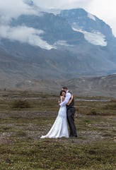 a bride and groom standing at the athabasca icefeilds