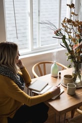 mulher em uma mesa com caderno café e difusor de óleos essenciais