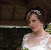 girl in an ivory vintage style wedding dress smiling with a pink floral bouquet in her hands