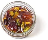 Top-down view of a little, clear, open container of fig conserve with pistachio, nuts, & dried fruit