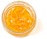 Top-down view of a little, clear, open container of orange marmalade with peel slices.