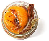 Top down view of a little, clear, open container of peach mostarda with mustard seeds & a bay leaf.