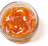 Top-down view of a little, clear, open container of orange mango chutney Chutneys