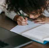"Small girl writing in a notebook, focused on her learning."