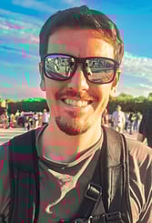 Portrait d’un homme souriant avec des lunettes de soleil reflétant une foule, ciel bleu et ambiance ensoleillée d’événement