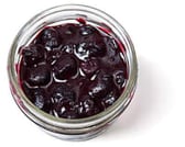 Top-down view of a little, clear, open container of thick and chunky blueberry compote.