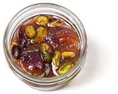 Top-down view of a little, clear, open container of fig conserve with pistachio, nuts, & dried fruit