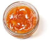 Top-down view of a little, clear, open container of orange mango chutney Chutneys