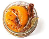 Top down view of a little, clear, open container of peach mostarda with mustard seeds & a bay leaf.