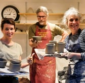 three people standing holding the pots they threw on the beginners course