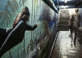 Blurred figures passing a painted underwater mural in a dimly lit pedestrian tunnel