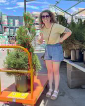 a woman in a yellow shirt is holding a plant tattoo artist being silly