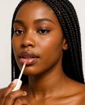 A black woman with braids applying lip gloss