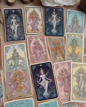 Three tarot cards are arranged in a row on a white surface, depicting a lion, a butterfly, and a tree with roots. Surrounding the cards are several crystals, including an amethyst cluster with a lit candle and various other gemstones.